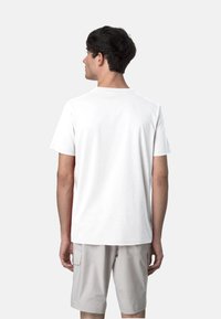 T-shirt bianca di cotone con maniche corte e scollatura rotonda, caratterizzata da una superficie liscia e un design semplice, indossata con pantaloni corti grigi chiari.