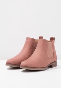 Rosa Wildleder-Stiefeletten mit elastischen Seitenpanels, einer abgerundeten Spitze und einem niedrigen, gestapelten Holzabsatz. Glatte Textur mit dezenten Stichdetails.