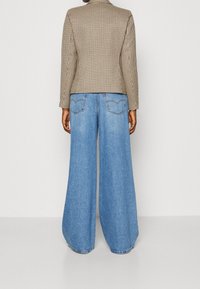 Brązowa kraciasta krótka marynarka w zestawie z szerokimi, jasnoniebieskimi dżinsami o luźnym kroju i standardowymi tylnymi kieszeniami.