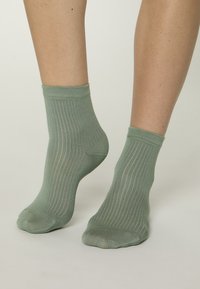 Calcetines tobilleros de color verde claro con textura acanalada y puño ajustado, que muestran sutiles líneas verticales a lo largo de la tela.
