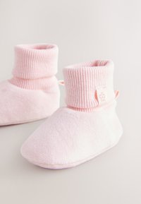 Chaussons doux rose pâle en tissu pelucheux avec un bord-côte replié. Ils présentent un petit motif floral et un bout lisse et arrondi.