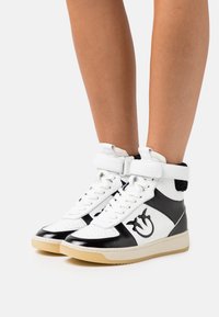 Höga sneakers i svart och vitt läder, med en vadderad ankelrem, texturerade detaljer och en logotyp på sidan. Gummiyttersula.