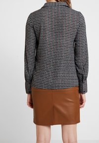 Blusa a maniche lunghe a quadri con un motivo marrone e blu, abbinata a una gonna in ecopelle marrone. Collo classico e vestibilità sartoriale.