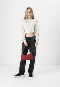 Red leather bag, cropped cream sweatshirt, black high-waisted jeans, black sneakers, standing against a white background.