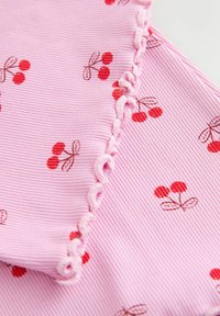 Vaaleanpunainen, poimuttunut kangas, jossa punainen kirsikkakuosi ja koristeellinen aaltoileva reuna. Pinta teksturoitu hienovaraisine uurteineen.