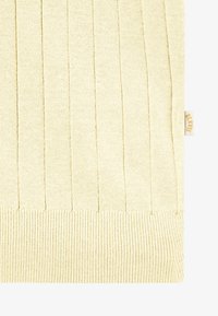 Tissu tricoté couleur crème avec côtes verticales et une petite étiquette latérale marquée "BLAKYS" en lettres dorées.