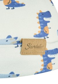 White fabric with blue and orange cartoon dinosaurs and a brown stitched label with "Sterntaler" embossed.
