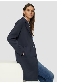 Cappotto navy doppiopetto con vestibilità su misura, tasche laterali e rever eleganti; tessuto in misto lana con una texture liscia.