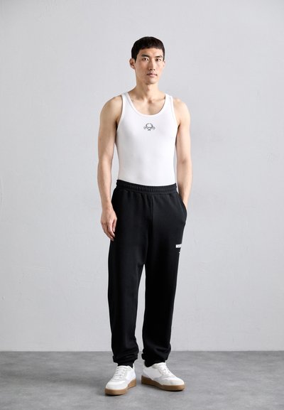 Vitt linne med en liten design, kombinerat med svarta sweatpants och vita sneakers med bruna detaljer. Slät tyg, avslappnad passform.