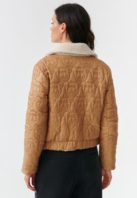Bruine gewatteerde jas met een gestructureerd berenpatroon, voorzien van een fluffy witte kraag en een kort ontwerp.