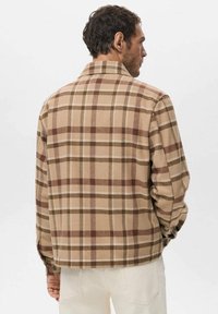 Chaqueta de cuadros marrón y beige con un acabado texturizado similar a la lana, que cuenta con cuello y puños con botones. Diseñada con un ajuste relajado.