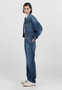 Jeans jakna s krojenjem iznad struka, dva džepa na prsima i širokim rukavima, u kombinaciji s širokim trapericama. Svijetloplava boja, ležeran stil.