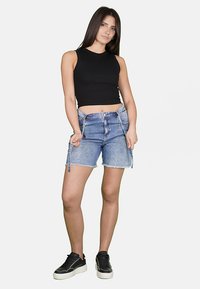 Top senza maniche nero, pantaloni shorts in denim azzurro chiaro con orlo sfrangiato e sneakers nere con suola bianca. Outfit semplice e casual.