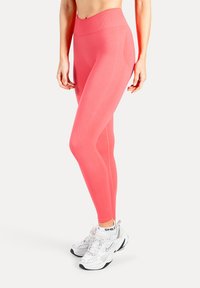 Rosa Leggings mit hoher Taille aus dehnbarem Material, mit Seitennähten, kombiniert mit weißen Sneakers.