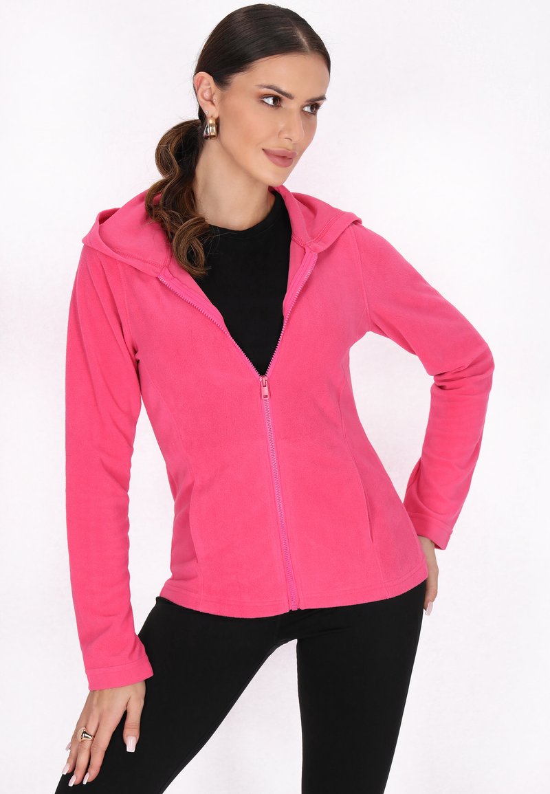 Giacca in pile rosa con zip e cappuccio, maniche lunghe e design slim fit. Presenta una zip frontale e una texture morbida. Indossata sopra una maglietta nera.