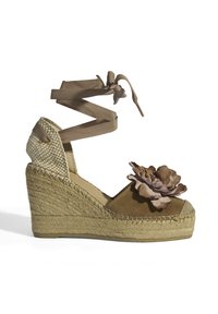 Braune Wildleder-Wedge-Sandale mit gewebtem Jute-Absatz, ausgestattet mit einem floralen Akzent und einem Schnürdesign um den Knöchel. Hellbraune Riemen und Sohle.