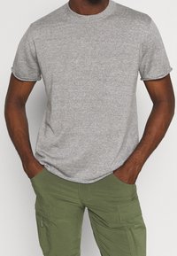 Grå kortärmad t-shirt i texturerad tyg med rundad halsringning, kombinerad med olivgröna cargobyxor med sidofickor.