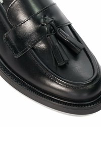 Black leather loafers featuring a smooth finish, decorative tassels, and a textured sole with detailed stitching along the edge.