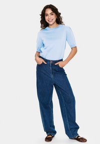 Top scurt de culoare albastru deschis, cu un finisaj texturat, asortat cu pantaloni largi din denim de culoare bleumarin și balerini maro.