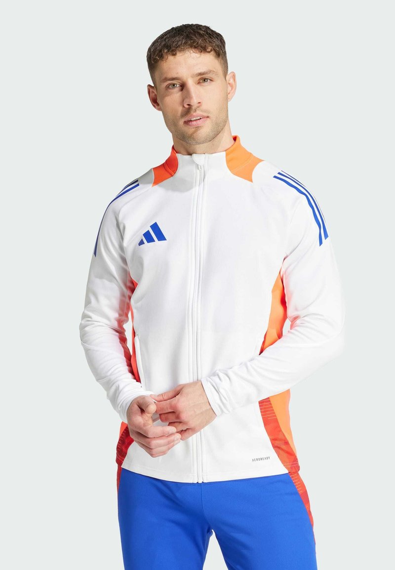 Giacca zip bianca sportiva con dettagli arancioni e blu, dotata di maniche lunghe e pannelli laterali testurizzati. Pantaloni sportivi blu.