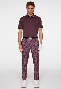 Bordowa koszulka polo z krótkim rękawem, w komplecie z bordowymi spodniami w wzory z białymi konturami. Do zestawu dołączone białe buty i rękawica golfowa.