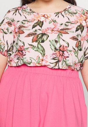 Bluzka z krótkim rękawem w kwiatowy wzór w pastelowych odcieniach, zestawiona z jasnoróżową spódnicą z wysokim stanem.