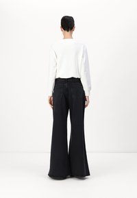 Witte langemouwen top met een ronde hals, gecombineerd met hoge taille, wijde zwarte jeans met achterzakken en een onafgewerkte zoom.