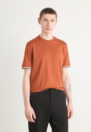 Kortærmet orange t-shirt med rund halsudskæring, der har sort-hvide stribede detaljer ved ærmeenderne. Fremstillet af bomuldsmateriale.