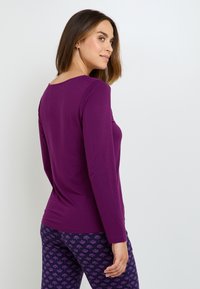 Haut à manches longues violet en tissu doux, coupe ample, col rond. Associé à un legging marine orné d'un motif floral dans des nuances de violet.