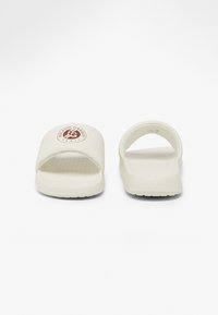 Sandales blanches à glissière avec une semelle texturée, design à bout ouvert et talon arrondi. Présentent un logo circulaire sur la bride avant.