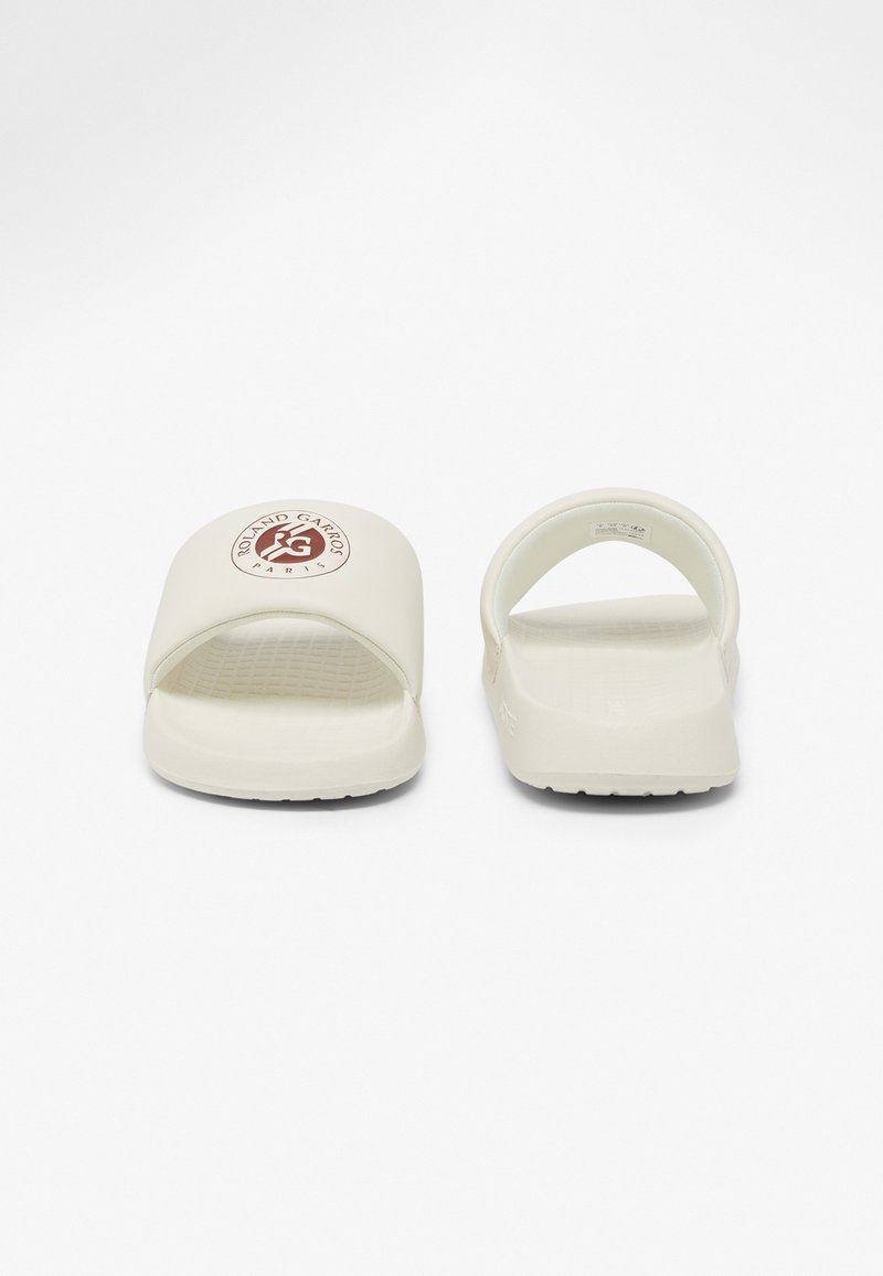 White slide sandals with a textured footbed, open toe design, and a rounded heel. Features a circular logo on the front strap.