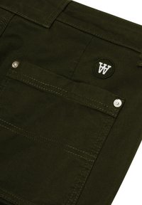 Olivenfarbene Cargo-Shorts mit einer Gesäßtasche mit silberner Hardware und einem weißen gestickten Logo. Der Stoff hat eine weiche, strukturierte Oberfläche.