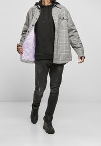Rudfarvet ydre skjortejakke med ternet mønster og lilla for, lagd over en sort hoodie, kombineret med sort slidte jeans og sorte høj-til-tå sneakers.