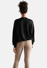 Sweatshirt noir surdimensionné avec un col rond, assorti à des leggings beige clair. Texture lisse, sans motifs ni éléments métalliques visibles.