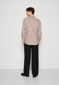 Camicia a maniche lunghe marrone e bianca con motivo, colletto a punta, polsini con bottoni e vestibilità comoda, abbinata a pantaloni neri a gamba larga.