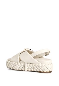 Bílé kožené sandály s pletenou podrážkou, designem křížových pásků, nastavitelným páskem kolem kotníku a hladkým povrchem.