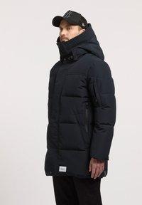 Jachetă puffer de culoare albastră închisă, cu guler înalt, buzunare cu fermoar și accente ribbed. Prezintă o închidere cu buton și un eticheta cu logo în partea de jos.