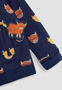 Felpa navy con un motivo ripetuto di mucche delle Highlands in stile cartone animato colorate; include una toppa di mucca texturizzata vicino alla tasca.