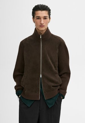 Giacca marrone con zip e colletto alto, realizzata in un tessuto morbido con maniche a costine. Texture liscia con tasche laterali, taglio comodo.