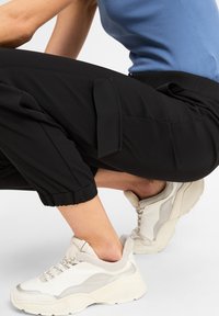 Schwarze cropped Hosen mit elastischen Bündchen, kombiniert mit beigen und weißen Chunky-Sneakers, die eine strukturierte Sohle und Schnürung haben.