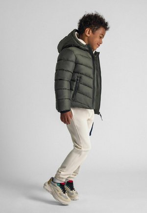 Dark green puffer jacket with a hood, zippered front, and quilted texture, paired with cream sweatpants and multi-colored sneakers.