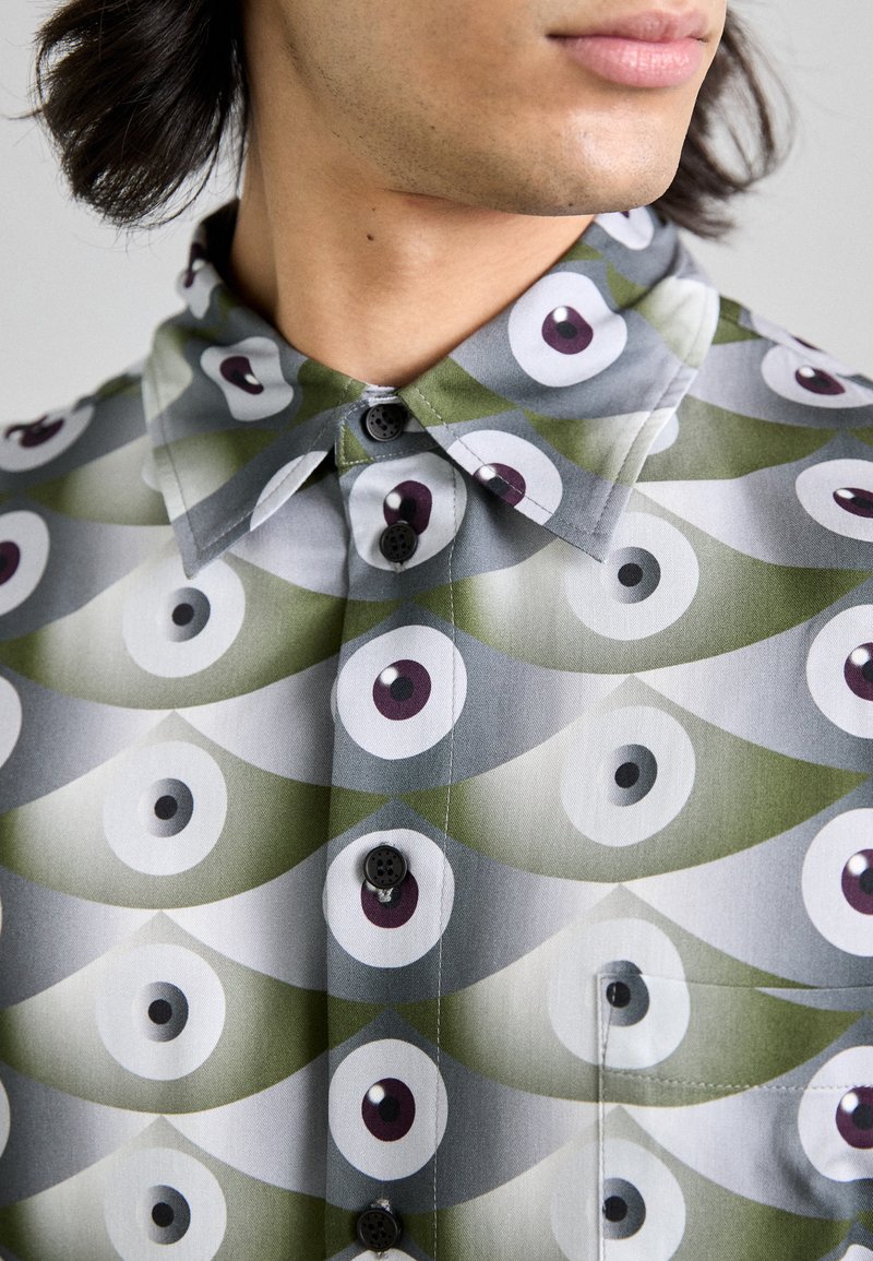 Knap-up skjorte med et geometrisk øje mønster i gråtoner og grøn. Fremstillet af stof med en glat tekstur og foldet krave.