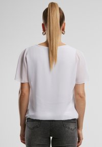 Blusa bianca a maniche corte con una texture morbida e liscia e scollatura tonda. Presenta una vestibilità ampia e dettagli di cucitura discreti sulle maniche.