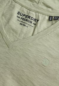Olivegrøn v-hals t-shirt lavet af blødt, let materiale. Har brandlogo i lys grøn broderet på brystet.