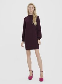 Vestido roxo de malha com gola alta e mangas longas ligeiramente bufantes, combinado com sapatos plataforma rosa brilhante. Estilo minimalista.