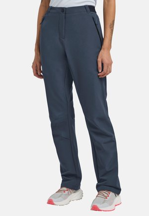 Personne portant un pantalon slim bleu foncé avec poches latérales zippées et des baskets blanches avec des accents roses.