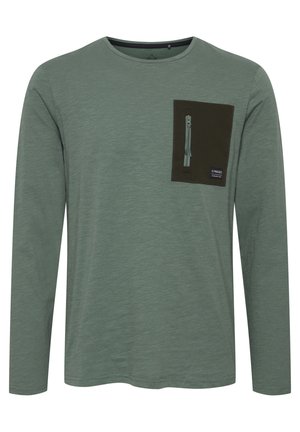 Long-sleeve, heathered green shirt featuring a dark green chest pocket with a zipper and tag, smooth texture, and round neckline.