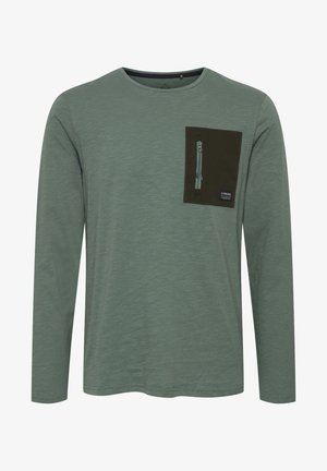 Long-sleeve, heathered green shirt featuring a dark green chest pocket with a zipper and tag, smooth texture, and round neckline.