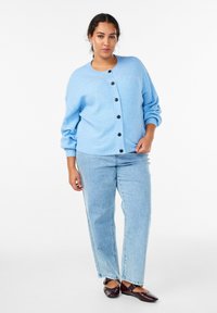 Svjetlo plava rebrasta vesta na kopčanje s crnim dugmadima, uparjena sa svjetlo plavim prugastim trapericama i smeđim ravnim cipelama. Jednostavan, opušten kroj.