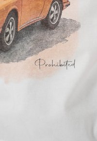 Nærbilde av bakhjulet på en oransje veteranbil med skygge og ordet "Forbudt" håndskrevet under på hvitt stoff.